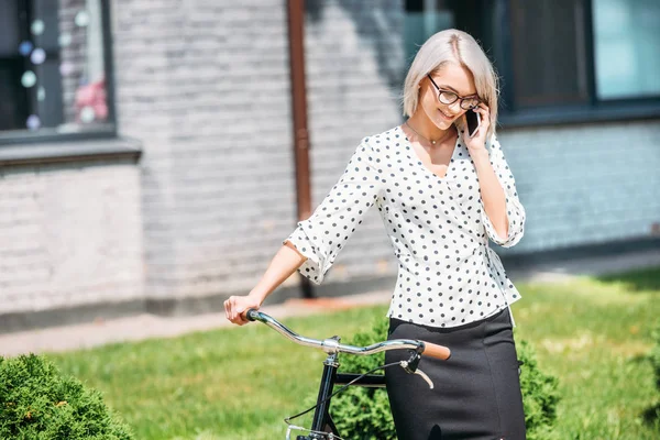 Портрет усміхненої бізнес-леді з ретро-велосипедом, що говорить на смартфоні на вулиці — стокове фото