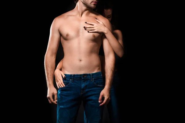 Visão parcial da mulher abraçando namorado sem camisa em jeans isolado em preto — Fotografia de Stock