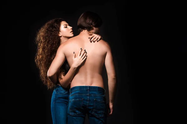 Back view of girlfriend hugging shirtless man isolated on black — Stock Photo