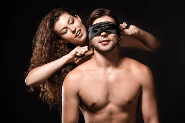 Retrato de mulher amarrando fita de seda em namorados olhos isolados em preto — Fotografia de Stock