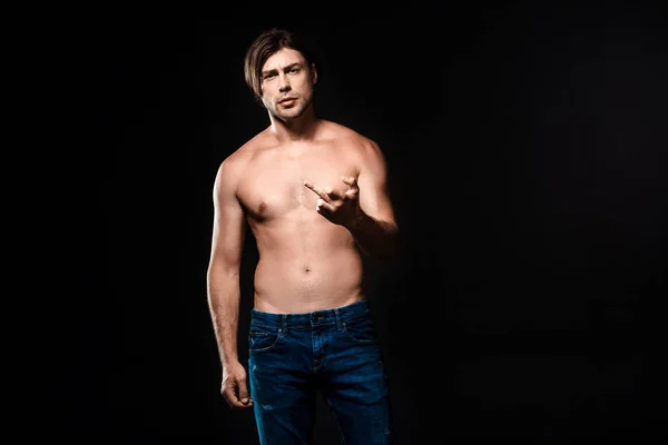 Portrait of shirtless man in jeans showing middle finger to camera isolated on black — Stock Photo