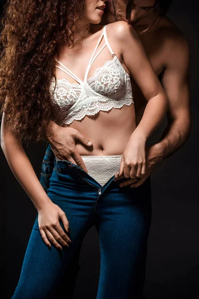 Cropped shot of man taking off girlfriends jeans isolated on black — Stock Photo