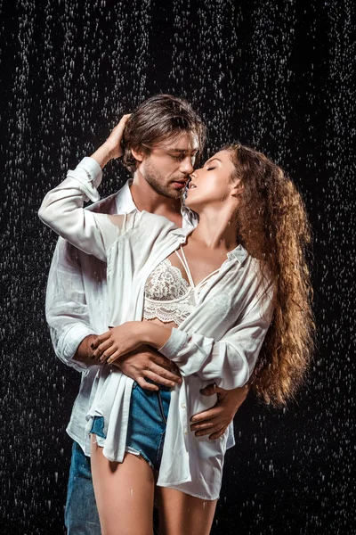 Retrato de casal sedutor abraçando sob chuva isolado em preto — Fotografia de Stock