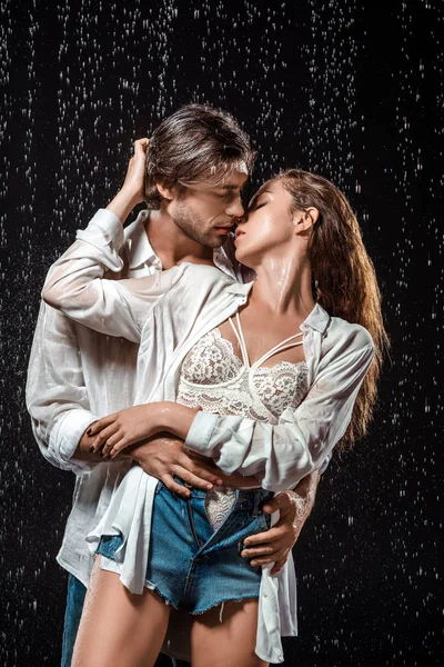 Портрет спокусливої пари, що обіймається під дощем ізольовано на чорному — стокове фото