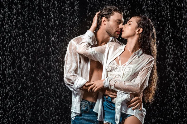 Portrait de couple séduisant étreignant sous la pluie isolé sur noir — Photo de stock