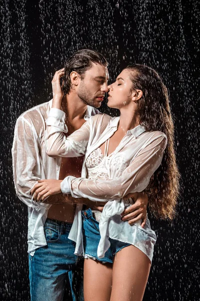 Retrato de casal sedutor abraçando sob chuva isolado em preto — Fotografia de Stock
