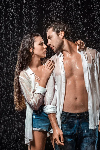 Portrait of sexy couple in white shirts standing under rain isolated on black — Stock Photo