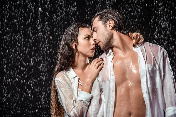 Portrait of sexy couple in white shirts standing under rain isolated on black — Stock Photo