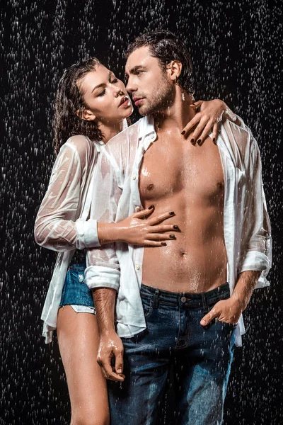 Sexy pareja en blanco camisas de pie bajo lluvia aislado en negro - foto de stock