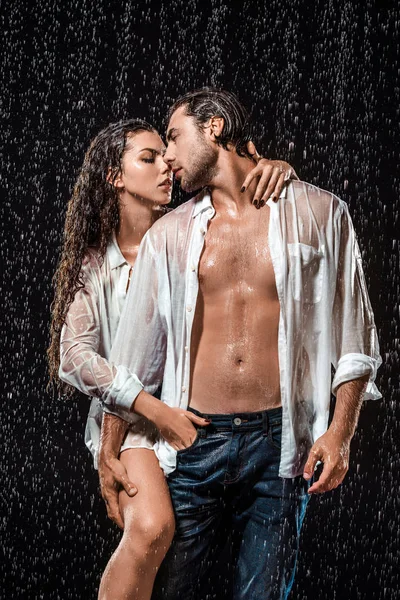 Sexy pareja en blanco camisas de pie bajo lluvia aislado en negro - foto de stock