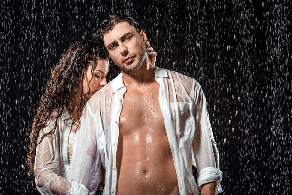 Sexy pareja en blanco camisas de pie bajo lluvia aislado en negro - foto de stock