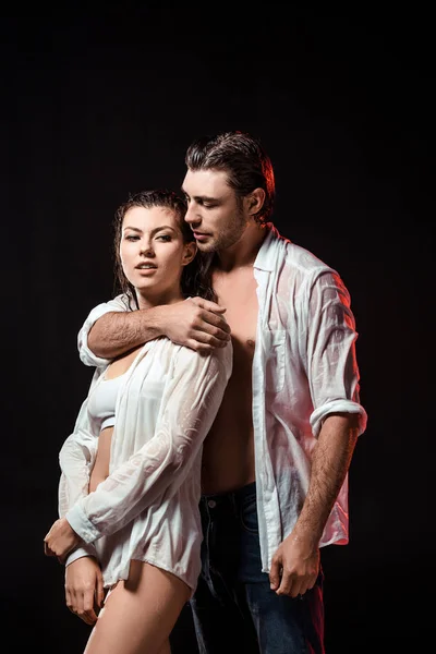 Portrait of seductive couple in wet white shirts posing on black backdrop — Stock Photo