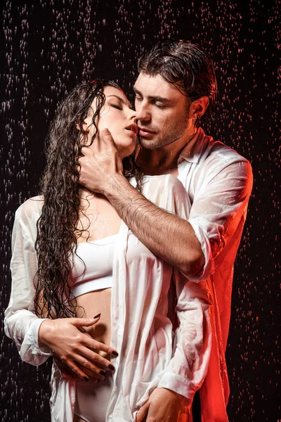 Retrato de pareja sexy en camisas blancas de pie bajo la lluvia sobre fondo negro - foto de stock