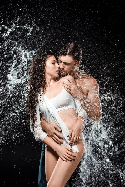 Retrato de sexy pareja joven con salpicadura de agua aislado en negro - foto de stock
