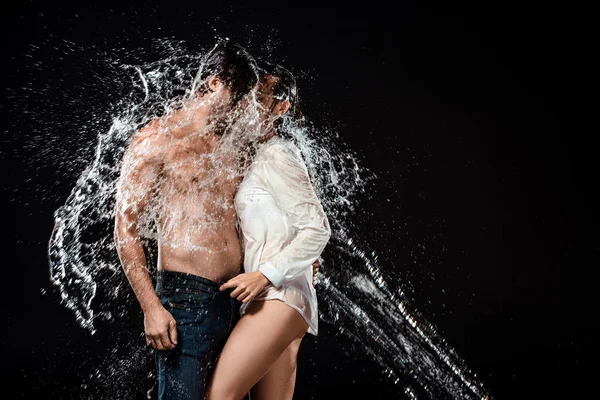 Vista lateral do casal sedutor com respingo de água isolado no preto — Fotografia de Stock