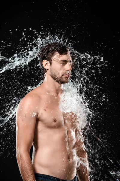 Vue latérale du jeune homme avec éclaboussure d'eau isolé sur noir — Photo de stock