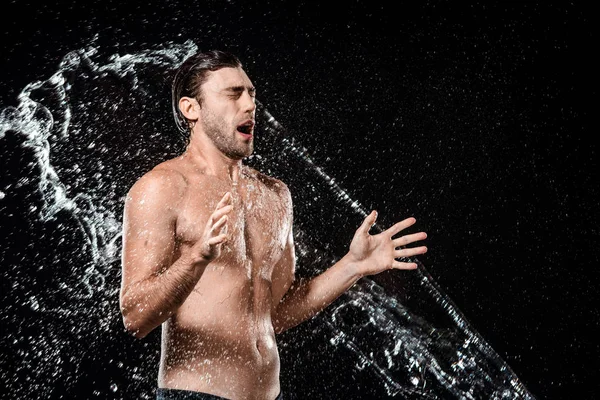 Vue latérale du jeune homme émotionnel swilled avec de l'eau isolée sur noir — Photo de stock