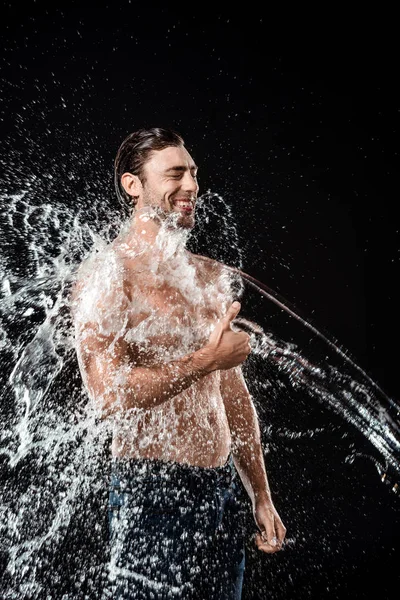 Smiling young man showing thumb up while swilled with water splash isolated on black — Stock Photo