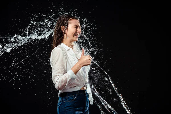 Vista lateral de la mujer sonriente en camisa blanca mostrando el pulgar hacia arriba mientras se hincha con agua aislada en negro - foto de stock