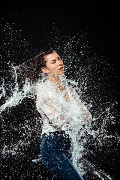 Vista lateral da mulher em camisa branca e jeans inchado com água isolada em preto — Fotografia de Stock