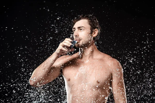 Porträt eines hemdlosen Mannes, der Wasser aus Glas trinkt, während er mit Wasser isoliert auf schwarz schwimmt — Stockfoto