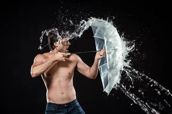 Vue latérale de l'homme torse nu avec parapluie avec éclaboussure d'eau isolé sur noir — Photo de stock