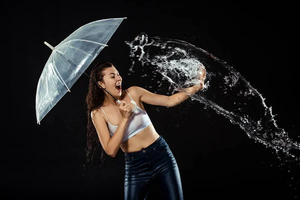 Giovane donna emotiva con ombrello strisciato con acqua isolata su nero — Foto stock