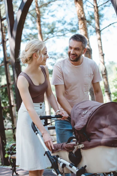 Parents heureux marchant avec la voiture de bébé dans le parc et se regardant — Photo de stock