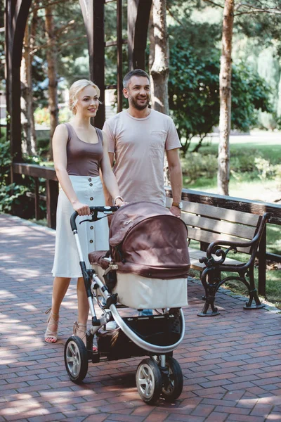 Parents marchant avec la voiture de bébé dans le parc le week-end — Photo de stock