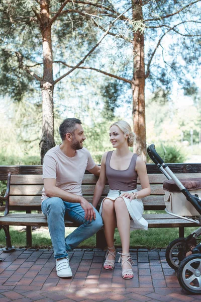 Parents sitting on bench near baby carriage in park and looking at each other — Stock Photo