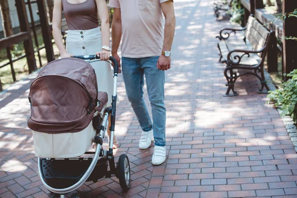 Imagen recortada de los padres caminando con carro de bebé en el parque - foto de stock