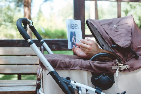 Cropped image of man holding cigarette and business newspaper in baby carriage — Stock Photo