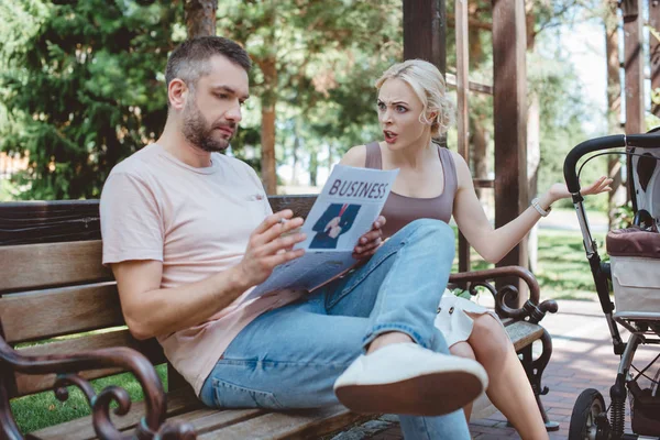 Husband smoking cigarette and reading newspaper near baby carriage in park, wife yelling at him — Stock Photo