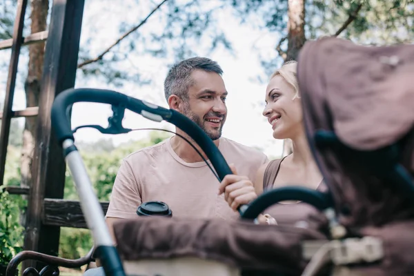 Parents assis sur le banc près de la voiture de bébé dans le parc et se regardant — Photo de stock