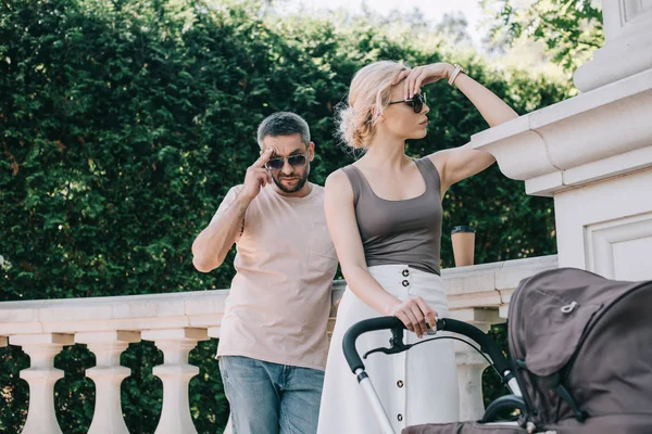 Angry parents touching heads and looking away near baby carriage in park — Stock Photo