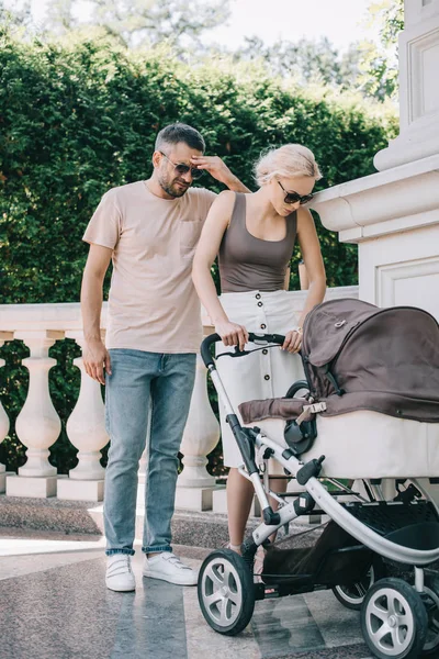 Exhausted parents standing near baby carriage in park — Stock Photo