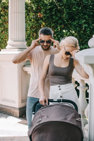 Irritated parents with headache standing near baby carriage in park — Stock Photo