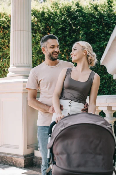 Husband hugging wife near with baby carriage in park and they looking at each other — Stock Photo