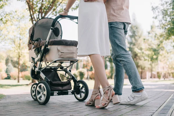 Imagen recortada de los padres caminando con carro de bebé en el parque - foto de stock