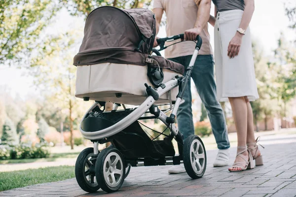Cropped image of mother and father walking with baby carriage in park — Stock Photo
