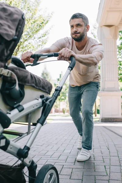 Father pushing heavy baby carriage in park — Stock Photo