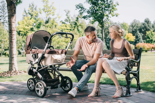 Parents quarreling on bench near baby carriage in park — Stock Photo