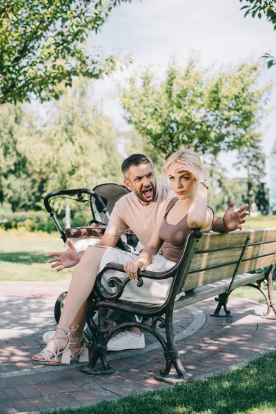 Marido gritando a la esposa y sentado en el banco cerca de carro de bebé en el parque — Stock Photo