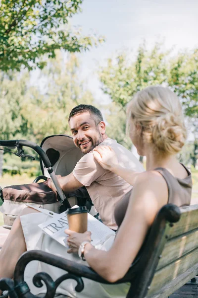 Femme assise près de voiture de bébé avec café pour aller et Voyage journal et en regardant mari — Photo de stock
