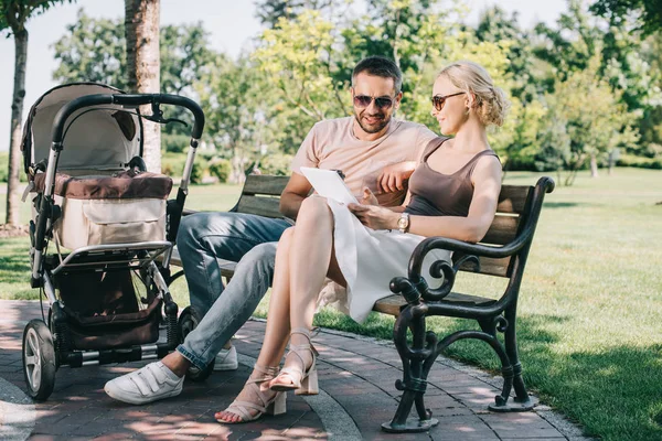 Parents assis sur un banc près d'un landau avec tablette — Photo de stock