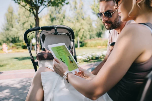 Eltern sitzen auf Bank neben Kinderwagen und schauen auf Tablet mit bester Einkaufsseite — Stockfoto