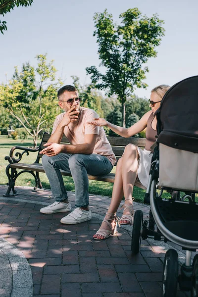 Père fumant la cigarette près de la voiture de bébé dans le parc, mère en colère pointant sur la cigarette — Photo de stock