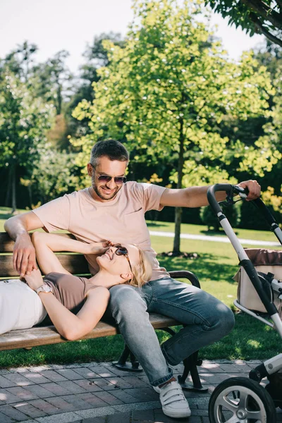 Wife lying on husband legs near baby carriage in park — Stock Photo