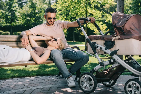 Moglie sdraiata sulle gambe del marito vicino alla carrozza del bambino nel parco — Foto stock