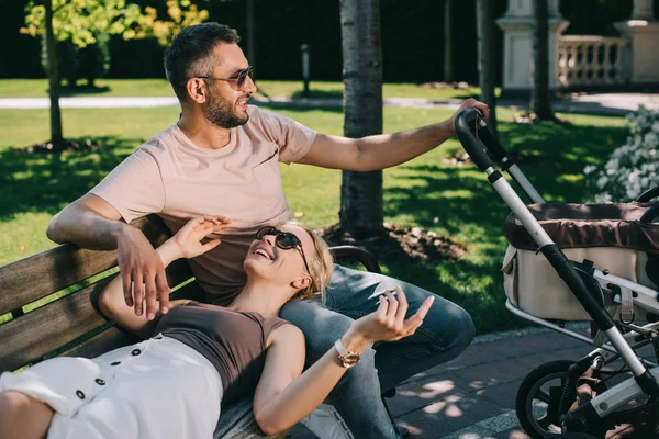 Wife lying on husband legs near baby carriage in park — Stock Photo